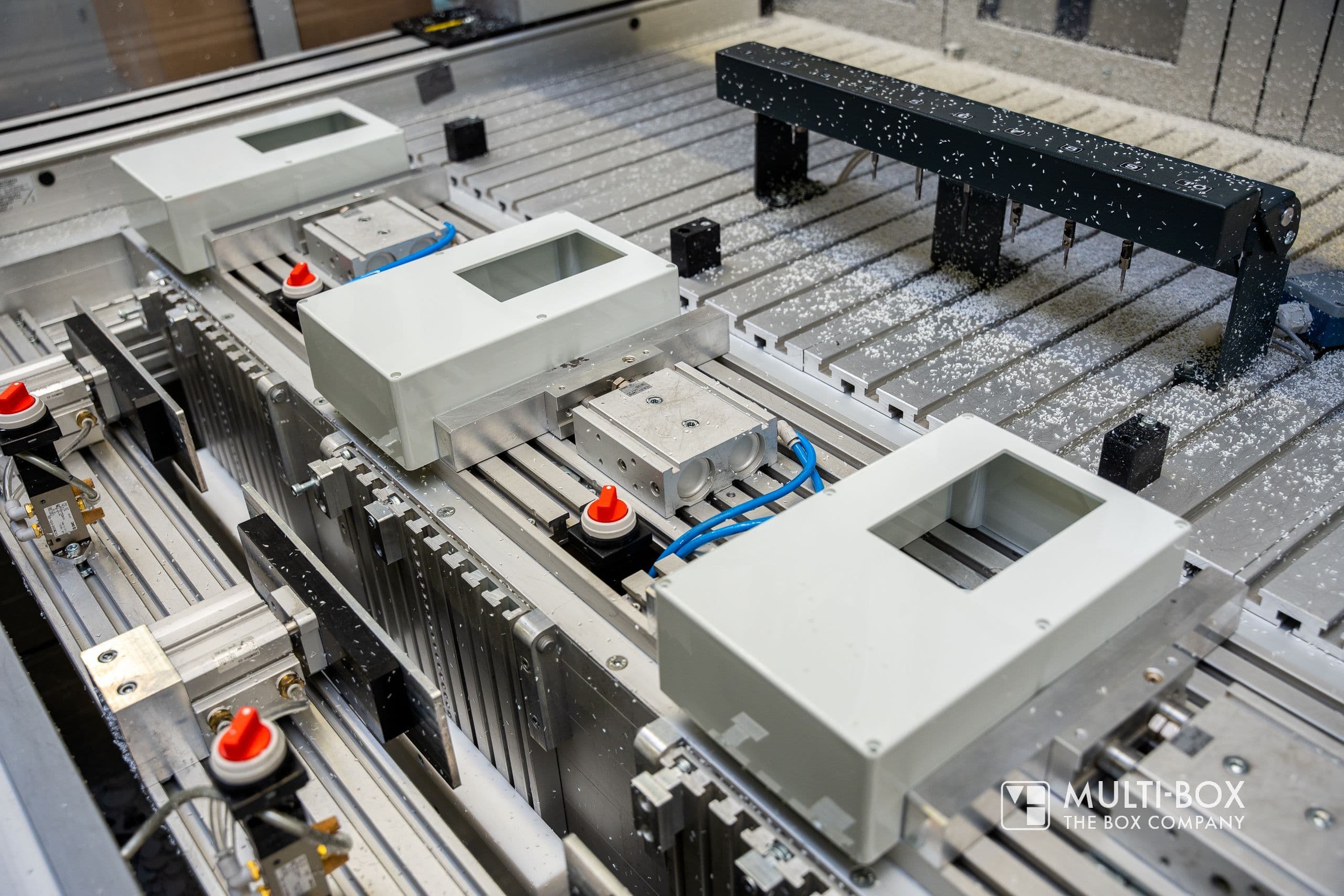 A CNC machine processes aluminum enclosures positioned precisely on the table.
