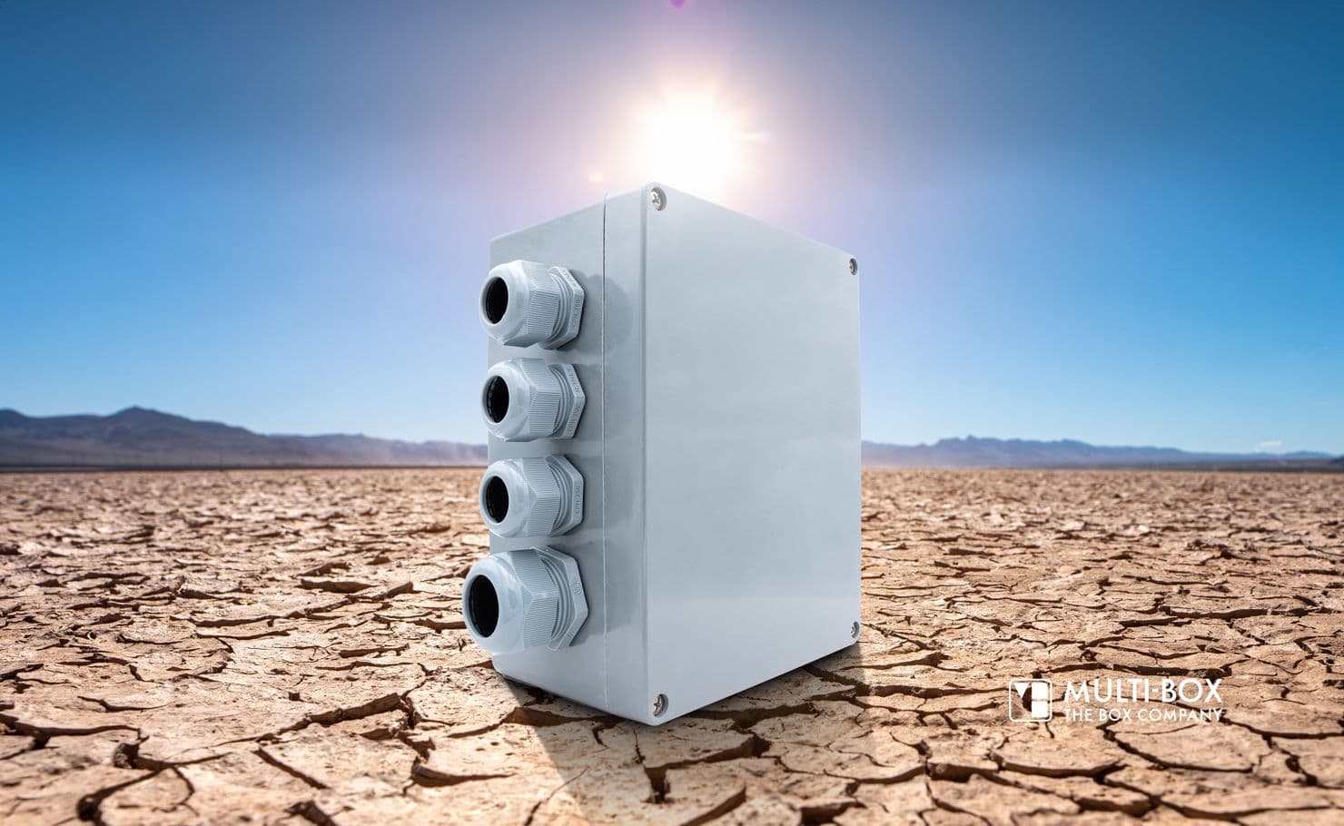 Wetterfestes Industriegehäuse von MULTI-BOX mit Kabelverschraubungen, platziert in trockener Wüstenlandschaft unter direkter Sonneneinstrahlung.