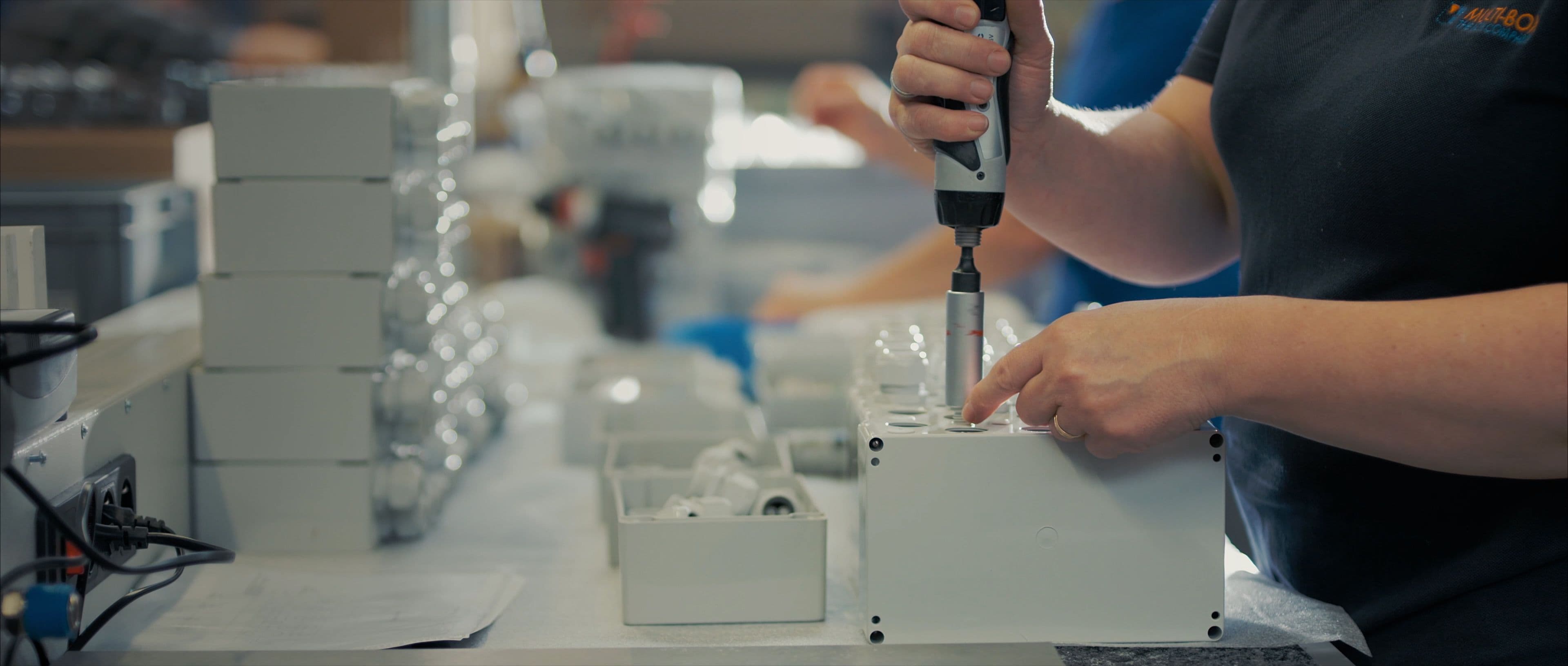 A person assembles enclosures using a tool while other enclosure parts are visible in the background.